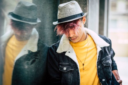 Photo for Sad and rebel teenager with alternative hair and casual clothes. Violet hairstyle for teenager with hat against a mirror in urban outdoor leisure activity alone. Concept of student and end of school - Royalty Free Image