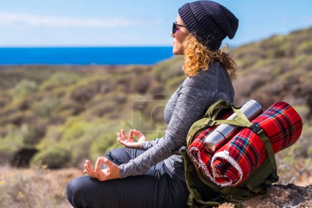 Photo for Zen and meditation activity in outdoor leisure lifestyle. Woman with backpack doing lotus position yoga. Concept of alternative healthy lifestyle and travel alone. Female people enjoying nature - Royalty Free Image