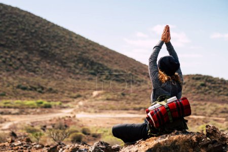 Téléchargez les photos : Vue arrière de femme aventure faisant du yoga position saine en face d'une montagne dans l'activité de trekking en plein air seul. Randonnée pédestre et méditation zen concept de style de vie. Les femmes voyagent alternative - en image libre de droit