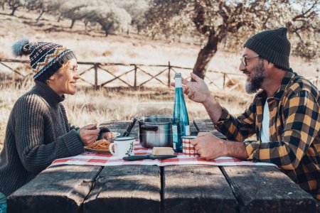 Photo for Couple of man and woman enjoying outdoor weekend leisure activity together eating on a wooden table at the park. Concept of healthy lifestyle in outdoors. Autumn season. Happy friends speak lunch - Royalty Free Image