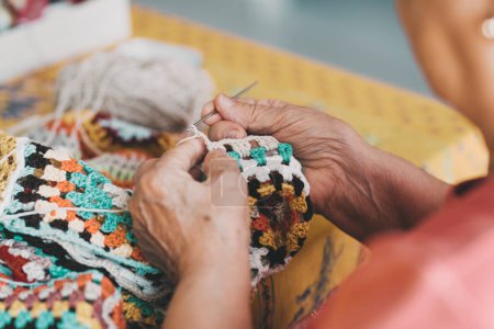 Téléchargez les photos : Gros plan des vieilles mains féminines qui font du tricot avec de la laine à la maison pour les loisirs en intérieur. Les retraitées âgées tricotent seules à la maison. Temps des personnes âgées et plaisir à l'intérieur en utilisant la laine et passe-temps - en image libre de droit