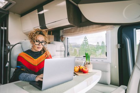 Photo for Independent woman sitting inside a camper van in smart remote working job activity using laptop. Concept digital nomad freedom lifestyle with female people writing on computer. Outdoors view outside - Royalty Free Image