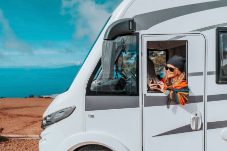 Photo for Woman enjoy arrival vacation travel destination after drive a big camper van motor home. Concept of happy female people in van life lifestyle. Summer journey. Planning road trip on mobile phone - Royalty Free Image