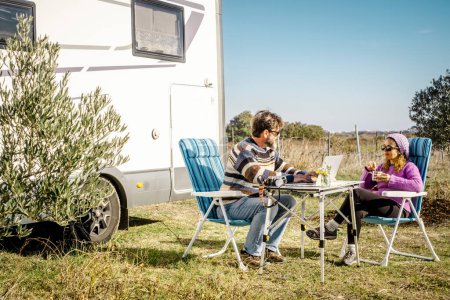 Photo for Happy tourist couple enjoy outdoor leisure activity sitting on the table with camper van in background. Alternative house lifestyle and nomadic vacation off grid. Travel with van man and woman people - Royalty Free Image