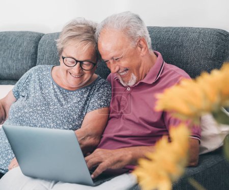 Téléchargez les photos : Vieux couple âgé utilisant ensemble un ordinateur portable assis sur le canapé surfer sur le web. Vous cherchez sur le web l'activité de concept de pages internet avec l'homme et la femme mûrs s'amuser et profiter de la technologie - en image libre de droit