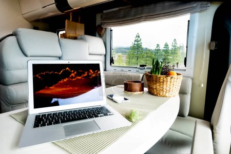 Alternative office and workstation for freedom smart working or digital nomad lifestyle concept. Laptop computer on a motor home table with nature and freedom view outside the window. Job activity