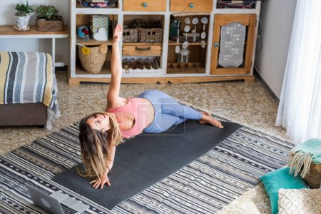 Téléchargez les photos : Femme sportive saine faisant des exercices pilates séance d'entraînement à la maison sur tapis de yoga sur le sol en regardant en ligne leçon de cours de tutoriel sur ordinateur et connexion Internet. Les gens modernes s'entraînent à l'intérieur seul - en image libre de droit