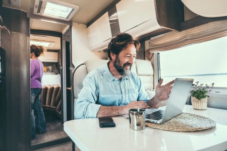 Photo for Man and woman living off grid inside a modern camper working on laptop connected online and enjoying freedom and vanlife lifestyle. Happy couple together on travel and vacation. Concept of holiday - Royalty Free Image