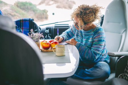 Photo for Travel vanlife lifestyle people concept. One woman having breakfast and writing road trip maps sitting inside the cabin of a modern camper van motorhome alone. Lady traveler and freedom concept - Royalty Free Image