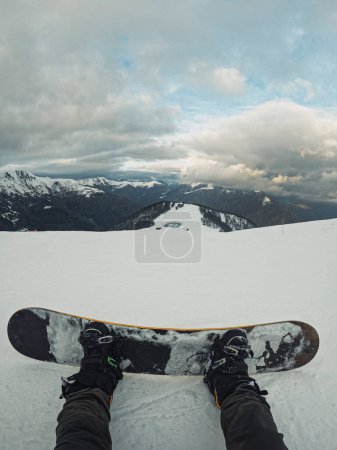 Téléchargez les photos : Vertical Pov man resting sitting on the snow with snowboard enjoying and admiring panorama landscape. Concept of winter mountains vacation and active sport people. Snow board rider in outdoor leisure - en image libre de droit