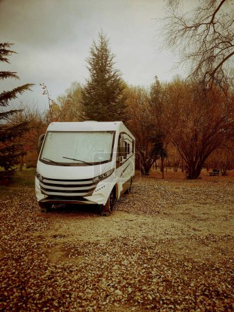 Foto de Autumn travel road trip concept with modern camper van parked on the leaves in the woods. Orange mood color old style filter. - Imagen libre de derechos