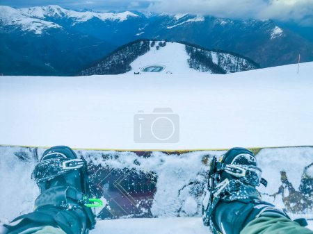Pov of man resting sitting on the snow with snowboard enjoying and admiring panorama landscape. Concept of winter mountains vacation and active sport people. Snow board rider in outdoor leisure
