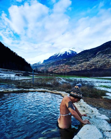 Téléchargez les photos : Woman tourist enjoying natural spa in winter mountains scenic place. Warm nature water with snow in background. Female tourist people enjoying thermal waters travel amazing alternative destination - en image libre de droit
