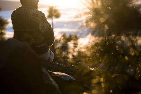 Photo for Man in outdoor leisure activity having relax time enjoying the sunset view sitting on the ground. Mountain and outdoors hiking travel. Amazing view with sunlight. Nature and people connection - Royalty Free Image