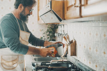 Photo for Adult man preparing food at home in the kitchen. Concept of male at work indoor. People in domestic lifestyle leisure activity. Happy husband prepare lunch for the family. Single adult daily life - Royalty Free Image