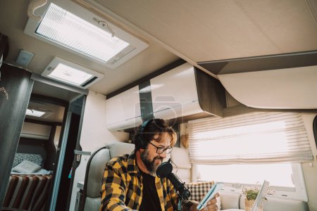 Photo for Traveler,  adult man speaking at the microphone in podcast recording business activity. Digital nomad and smart working inside a camper van. People at work in alternative office desk - Royalty Free Image