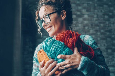 Téléchargez les photos : Woman with pleasure expression on face holding with love a bunch of wool balls in different color. Concept of indoor leisure activity and hobby. Female people like to work and knit. Happiness - en image libre de droit