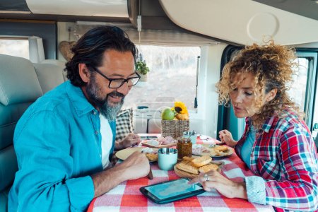Photo for Couple man and woman inside a camper van planning the next travel destination together using GPS modern device on the table. Lunchtime on vehicle motor home alternative adventure vacation. Lifestyle - Royalty Free Image