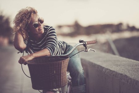 Téléchargez les photos : Woman smile and enjoy outdoor leisure activity alone having relax on her bike. Happy female people smile and look wearing sunglasses. Healthy transport lifestyle people sustainability - en image libre de droit