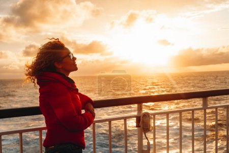 Téléchargez les photos : People enjoying travel and adventure lifestyle. One woman on ferry ship boat enjoy sunset ,smiling and relaxing. Tourist on the ocean transport. Summer trip vacation. Sea surface. - en image libre de droit