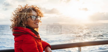 Téléchargez les photos : Woman enjoying sunset on travel at sea. Traveler happy woman in red jacket looking at ocean relaxing on luxury cruise liner boat. People and ferry boat transport. Travel activity - en image libre de droit