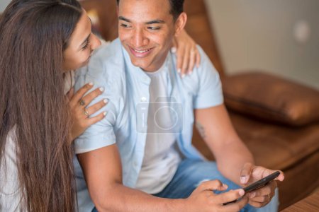 Téléchargez les photos : Couple in love resting on comfy couch having fun using smartphone apps, enjoy distant video call, wife showing interesting website to husband, choosing services goods on-line e-commerce usage concept - en image libre de droit