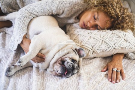 Téléchargez les photos : Dog and people sleeping together at bed viewed from above. Concept of love animal and best friend forever. One woman asleep on bed with puppy. Adorable pug domestic lifestyle female owner - en image libre de droit