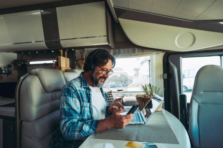 Photo for Traveler, modern online people job business lifestyle. One happy mature man using phone and computer inside a camper van motor home vehicle. Vacation travel and roaming connection technology worker - Royalty Free Image