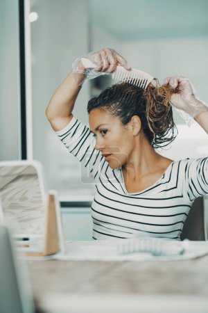 Foto de Woman applying care hair beauty products on her head at home. Independent lifestyle, female mature people concept. One female people using hairstyle treatment alone indoor. - Imagen libre de derechos