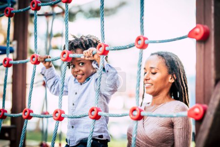 Foto de Afro-American  family mother and son enjoying time together at the playground park having fun. Mommy and child smiles outside - Imagen libre de derechos