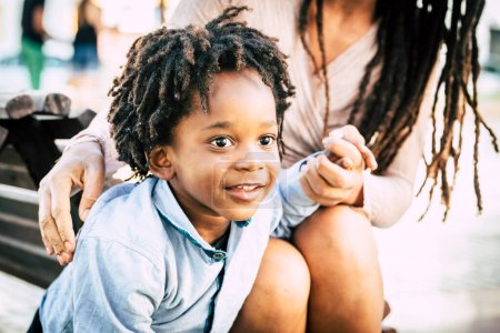 Foto de Portrait close up of little boy enjoying time outdoor with his mommy. Family with black mother and son in outdoors leisure activity. Children smiling. Afro-American - Imagen libre de derechos