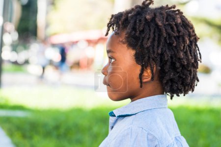 Photo for Side portrait of young children black ethic afro american diversity with green playground park in background. Dredd hair style little boy alone side view - Royalty Free Image