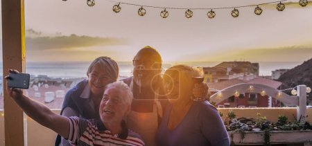 Téléchargez les photos : Groupe d'amis aînés profitant de loisirs en plein air prendre des photos selfie à l'extérieur à la maison en s'amusant et souriant. Technologie des personnes âgées partageant des photos, mode de vie des gens matures. Célébration coucher de soleil - en image libre de droit