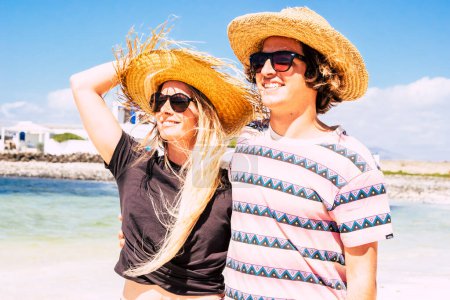 Photo for Cheerful young boy and girl smile together at the beach in summer tourism holiday vacation. Straw hats. Travel couple with sun on face. Happy people in relationship outdoor leisure activity and fun - Royalty Free Image