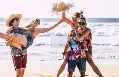 Téléchargez les photos : Groupe d'amis touriste profiter de l'été ludique activités de loisirs de plein air et des vacances à la plage portant les filles dans le dos et riant beaucoup ensemble dans l'amitié. - en image libre de droit