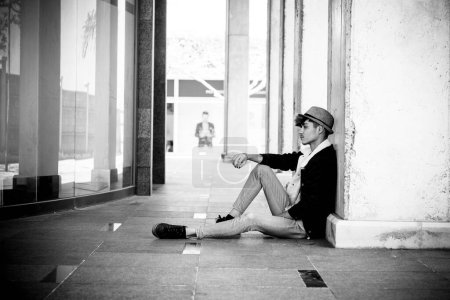 Téléchargez les photos : Un adolescent désespéré assis sur le sol en plein air. Dépression juvénile, jeune homme attentionné. Garçon seul dans la pauvreté. Les étudiants fatigués et épuisés par le travail scolaire. Concept de tristesse - en image libre de droit