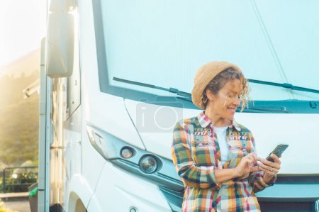 Photo for Woman driver enjoy camper parking rv area using phone app to plan next destination of travel. Happy tourist with van vehicle and roaming connection mobile technology. Traveler motor home lifestyle - Royalty Free Image