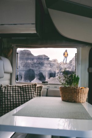 Photo for Modern explorer people lifestyle concept. Travel in scenic destination with motor home, Vanlife traveler. One man standing on a peak viewed from inside a camper van. Concept of nomadic life tourism - Royalty Free Image