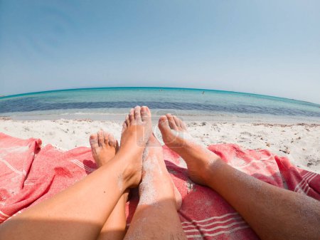 Téléchargez les photos : Pov de quelques pieds profitant de la plage et du soleil pendant les vacances d'été à la plage avec fond calme des yeux de poisson de mer. Les gens de tourisme et de détente reposant sur le sable. Bain de soleil nudisme homme et femme - en image libre de droit