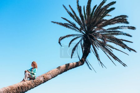 Foto de Turista sentada en una palmera en un viaje tropical destino de vacaciones de verano. Las mujeres se relajan en el increíble parque escénico. Estilo turístico. Chica de ocio al aire libre - Imagen libre de derechos