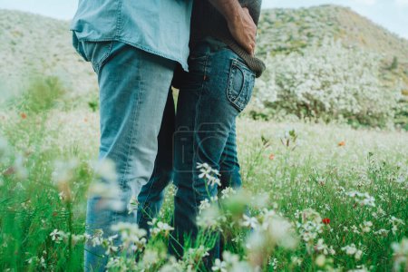 Foto de Romántica actividad de ocio al aire libre y pareja enamorada abrazándose y besándose en medio de verdes flores de primavera prado. Gente disfrutando de la naturaleza y la relación romántica juntos. Vacaciones. - Imagen libre de derechos