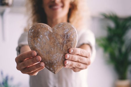 Photo for Happy female showing a handmade wooden heart at the camera. Concept of love and artisan decoration shabby chic style. Happiness and lifestyle person. Copy space indoor image - Royalty Free Image