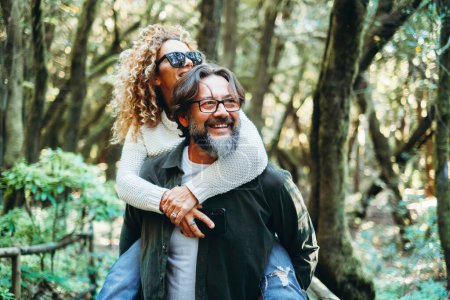 Photo for Adult man and woman in love and relationship enjoy weekend activity in outdoor leisure together. Carrying in piggyback. Youthful mature people playing and having fun looking the nature around. Holiday - Royalty Free Image