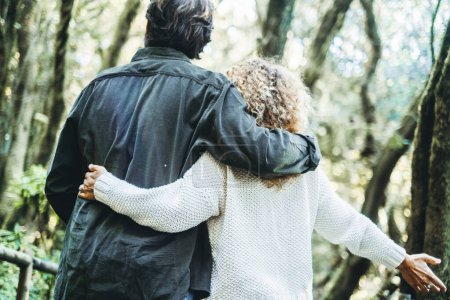 Photo for Back view of man and woman bonding and hugging enjoying outdoor leisure activity in scenic nature destination forest with high green trees. Couple of tourist enjoying travel destination. Together love - Royalty Free Image