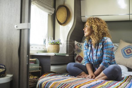 Photo for Woman and relax indoor leisure activity alone. One female people sitting on bedroom inside camper van and looking outside the window. Travel and serene, happy lifestyle people. Healthy mindful vanlife - Royalty Free Image