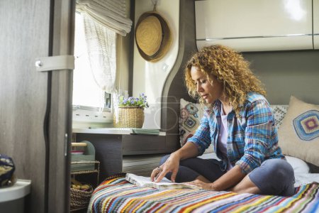 Photo for Camper van travel nomadic lifestyle people concept with serene woman reading a book sitting on bed in motorhome bedroom. Vanlife freedom lifestyle. New normal tiny house living off grid people life - Royalty Free Image