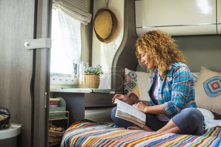 Photo for One woman reading a book sitting inside a modern camper van motor home and enjoy relax indoor leisure activity alone. Independent lady living off grid vanlife lifestyle. Travel and people relaxation - Royalty Free Image