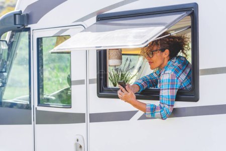 Photo for Travel and mobile roaming phone connection.  modern woman staying outside the window of her camper van rv and using cellphone to message remote friends. Living vanlife. Tourist and vehicle concept - Royalty Free Image