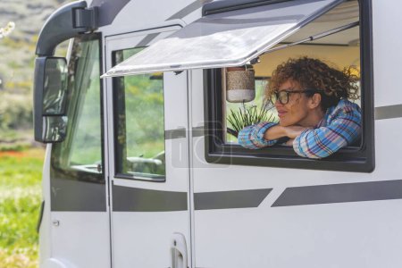 Photo for Serene tourist adult woman enjoy peaceful destination travel looking outside the window of camper van rv vehicle motor home and smiling. Vehicle transport and vacation lifestyle people. Dreaming happy - Royalty Free Image