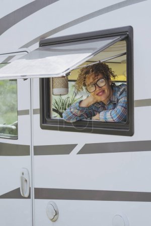 Photo for Portrait of happy tourist traveling on camper van vehicle and enjoying freedom travel vacation lifestyle concept. Cheerful young woman looking outside the window of tiny house motor home. Vanlife happy - Royalty Free Image